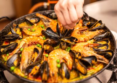 Eine Person fügt Gewürze zu einer großen Paella mit Garnelen und Muscheln hinzu.